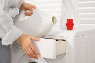 Woman pouring laundry detergent into washing machine indoors, closeup