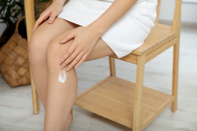 Photo of Young woman applying body cream on leg indoors, closeup