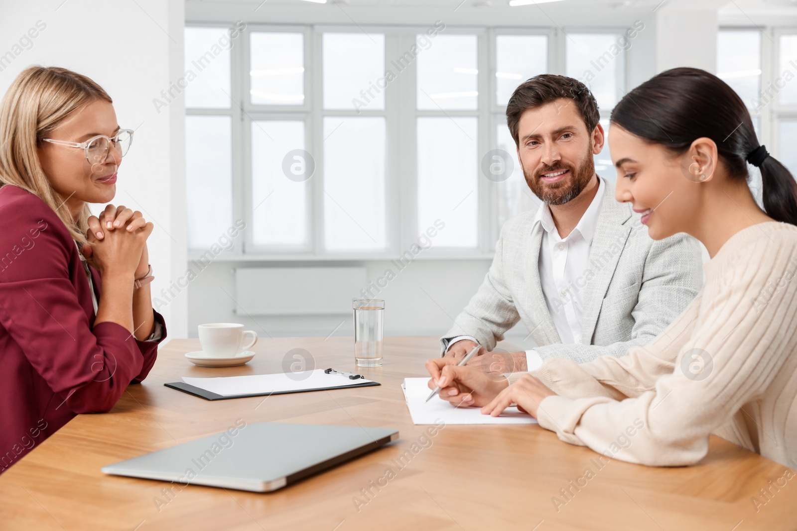 Photo of Real estate agent and couple signing contract at table in new apartment