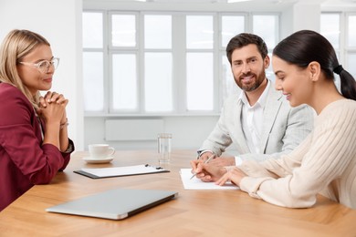 Photo of Real estate agent and couple signing contract at table in new apartment