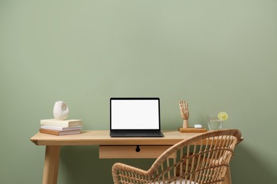 Stylish workplace with laptop, books and decor on table near light green wall