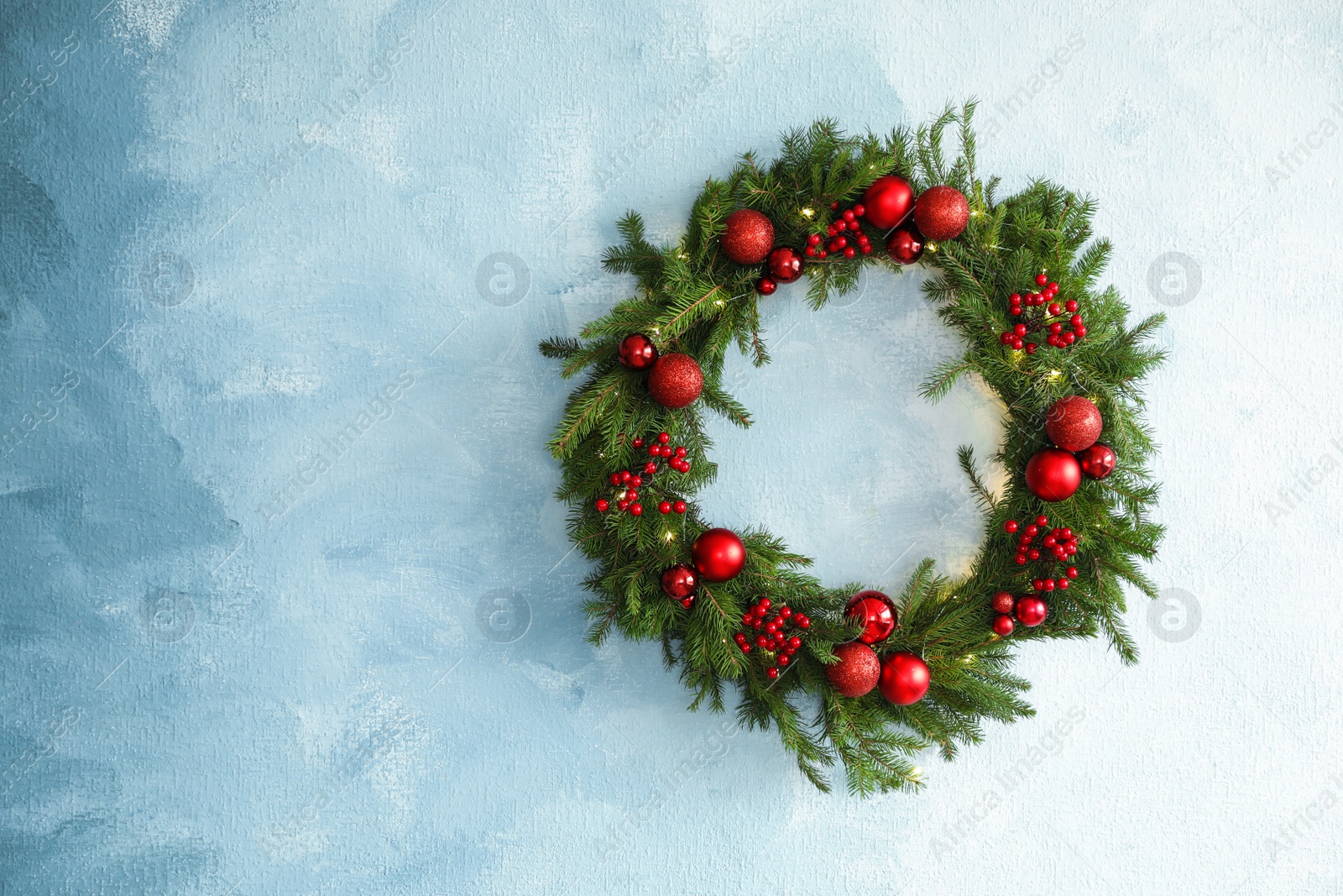 Photo of Beautiful Christmas wreath with festive decor on light blue wall, space for text