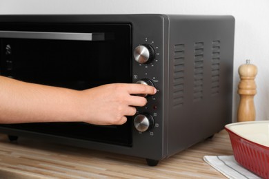 Woman adjusting temperature on electric oven indoors, closeup