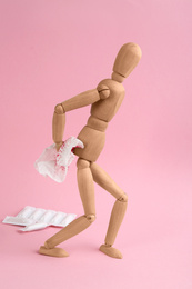 Photo of Wooden human figure and sheet of toilet paper with blood on pink background. Hemorrhoid problems
