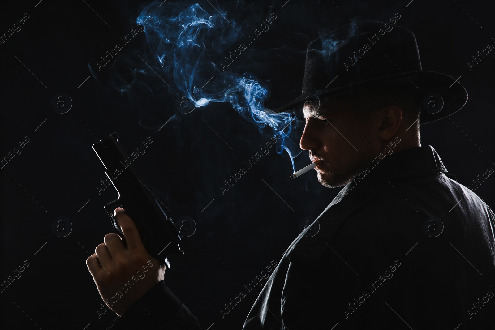 Photo of Old fashioned detective with gun smoking cigarette on dark background