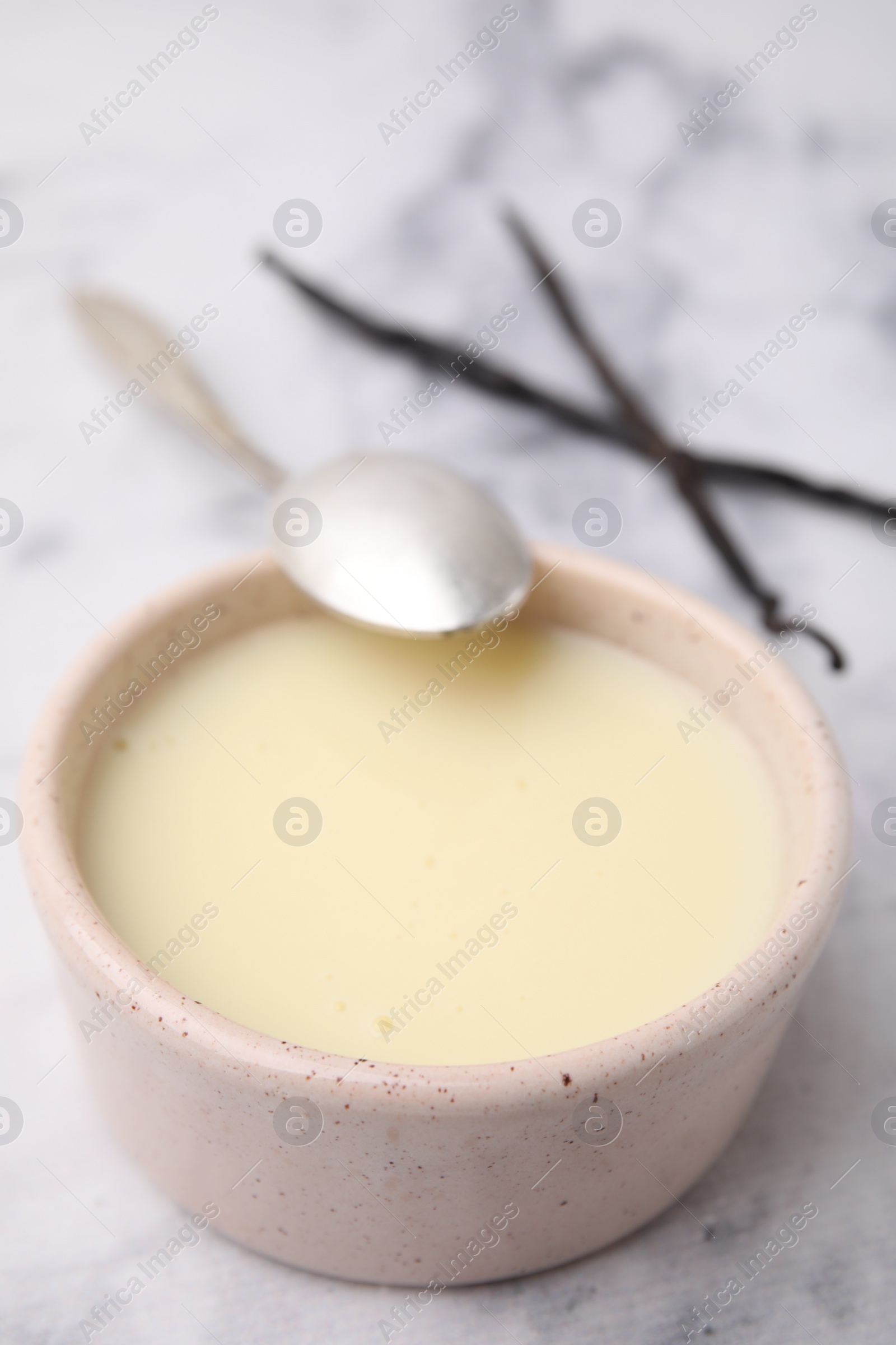 Photo of Bowl with condensed milk, vanilla pods and spoon on white marble table, closeup