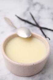 Photo of Bowl with condensed milk, vanilla pods and spoon on white marble table, closeup