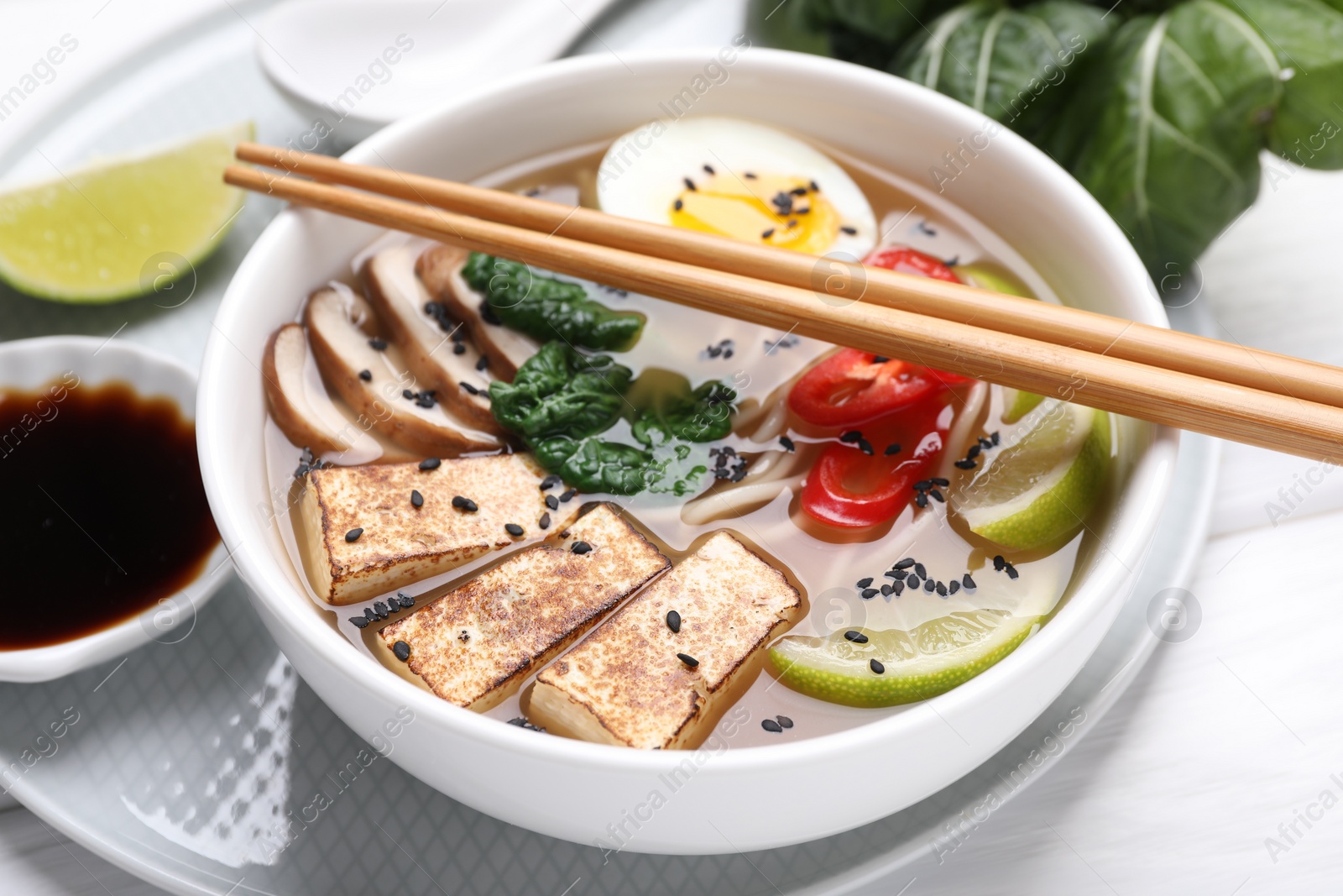 Photo of Delicious vegetarian ramen in bowl and chopsticks on white table, closeup