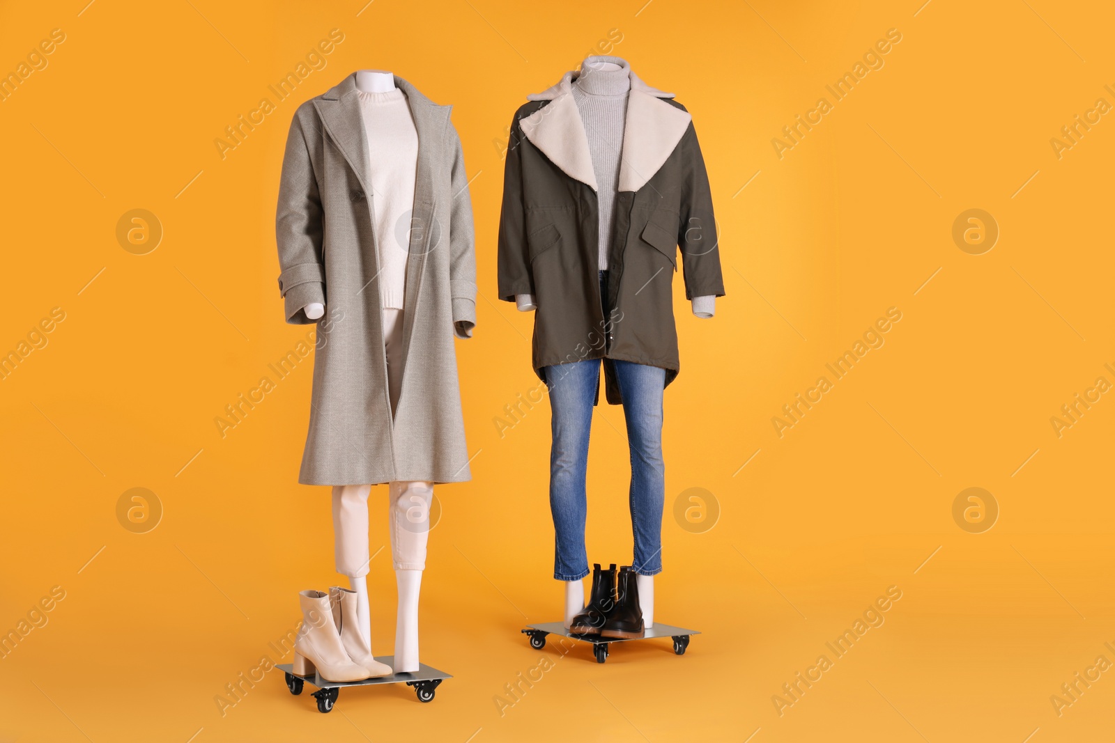 Photo of Mannequins with boots dressed in stylish coat, jacket, sweater and turtleneck on orange background