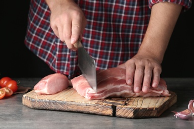 Photo of Man cutting fresh raw meat on table against dark background, closeup