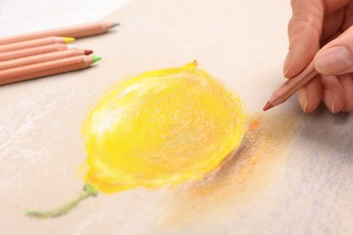 Woman drawing lemon on paper with pastel pencil at table, closeup