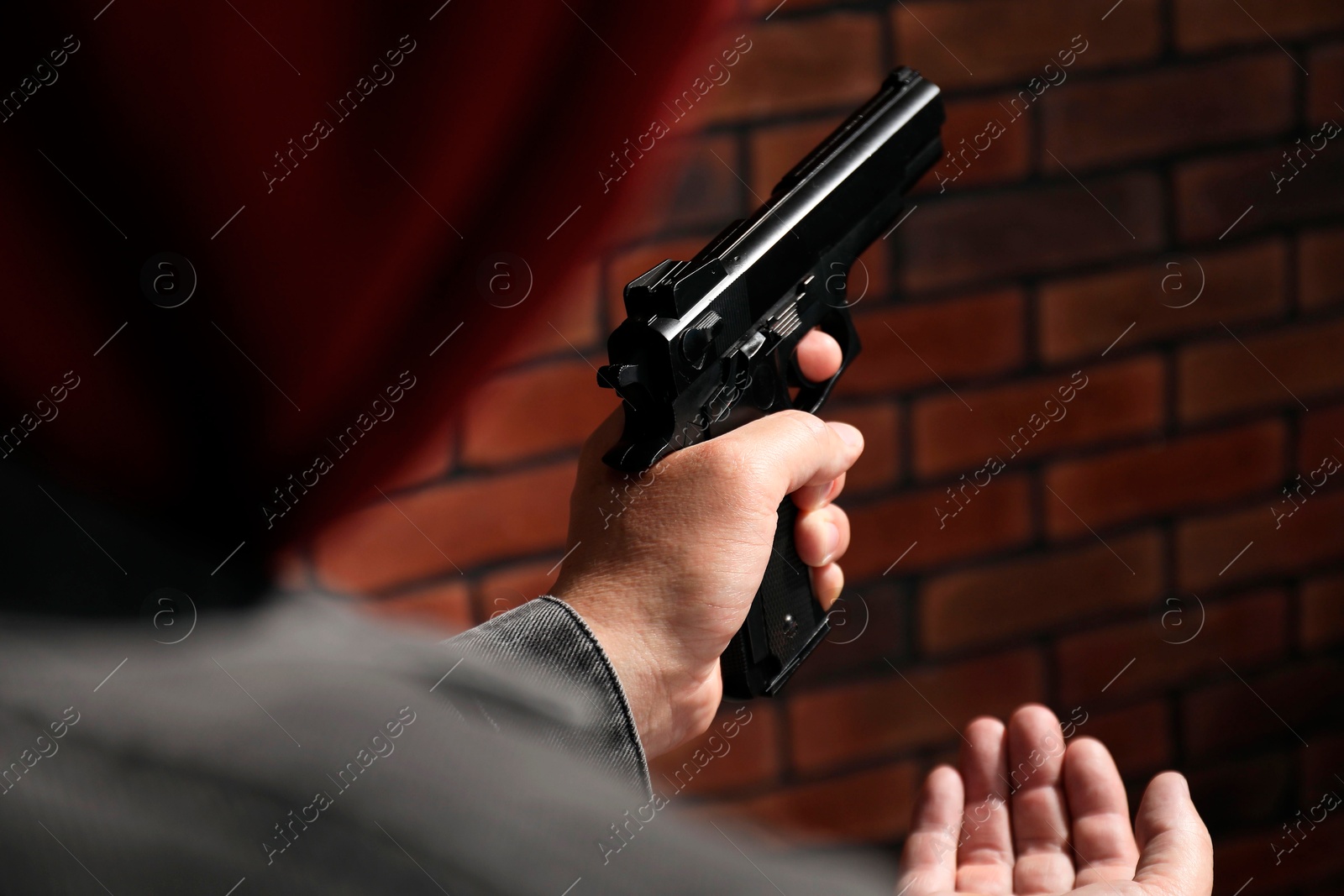 Photo of Dangerous criminal with gun near brick wall, closeup. Armed robbery