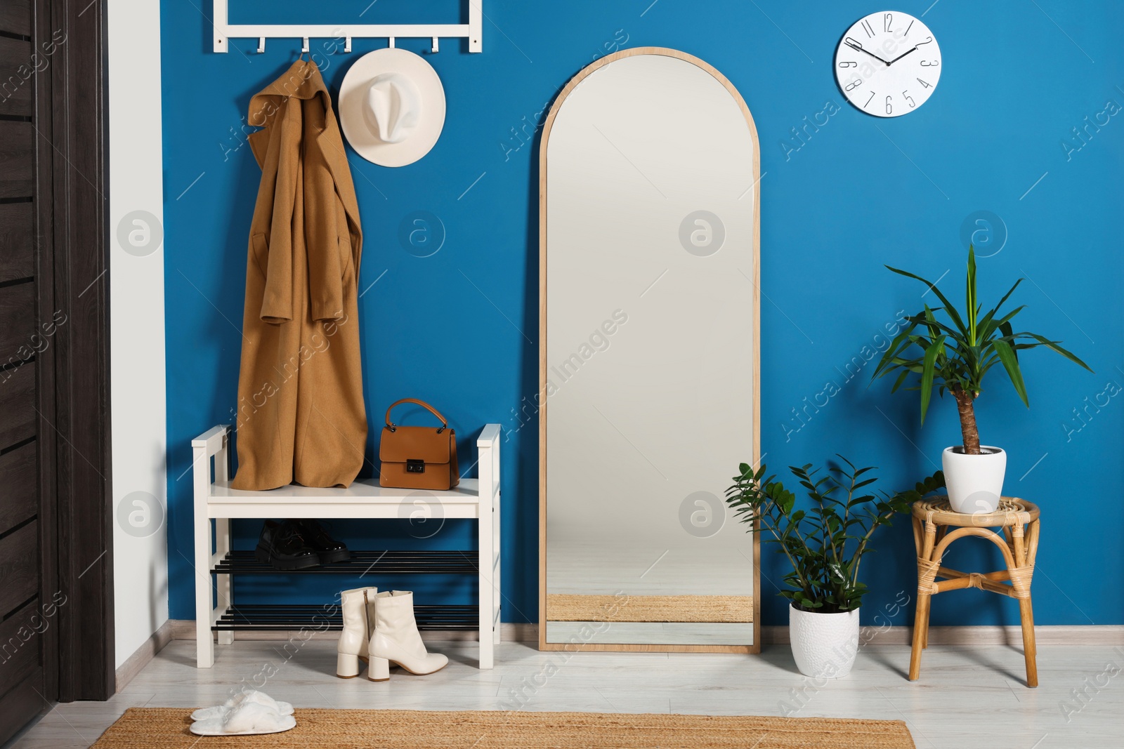 Photo of Stylish hallway with shoe storage bench and mirror near blue wall. Interior design