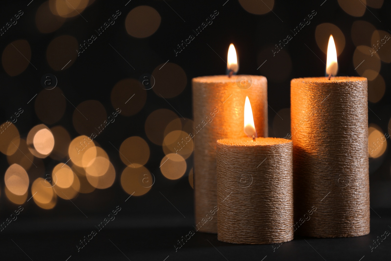 Photo of Burning gold candles against blurred lights in darkness. Space for text