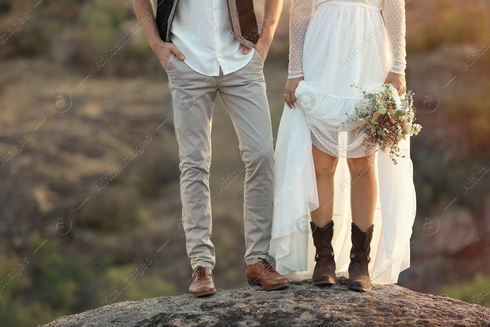 Photo of Happy newlyweds with beautiful field bouquet standing on rock outdoors, closeup