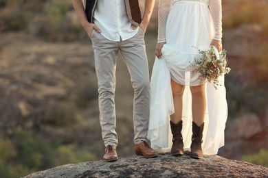 Happy newlyweds with beautiful field bouquet standing on rock outdoors, closeup