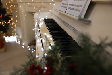 Photo of White piano with fairy lights indoors, closeup. Christmas music