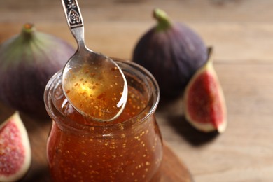 Tasty fig jam flowing down into glass jar and fresh fruits on table, closeup. Space for text