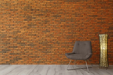 Photo of Grey modern chair and lamp near brick wall. Modern room interior