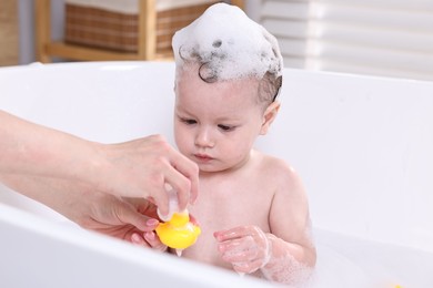 Mother bathing her cute little baby in tub at home