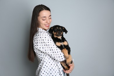 Young woman with cute puppy on light grey background. Space for text