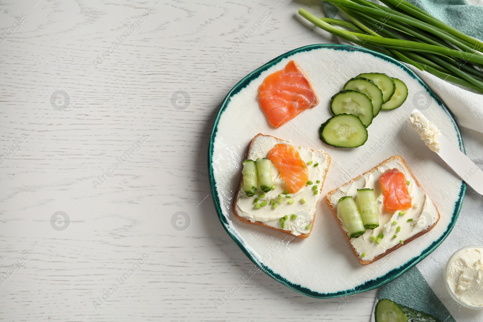 Photo of Toasted bread with cream cheese, salmon and cucumber on white wooden table, flat lay. Space for text