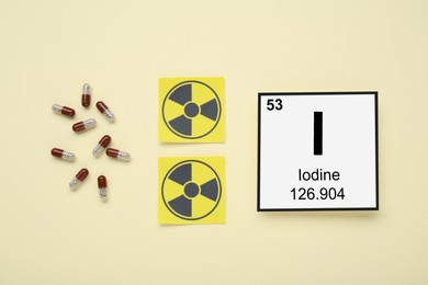 Photo of Card with chemical element Iodine, pills and radiation signs on beige background, flat lay