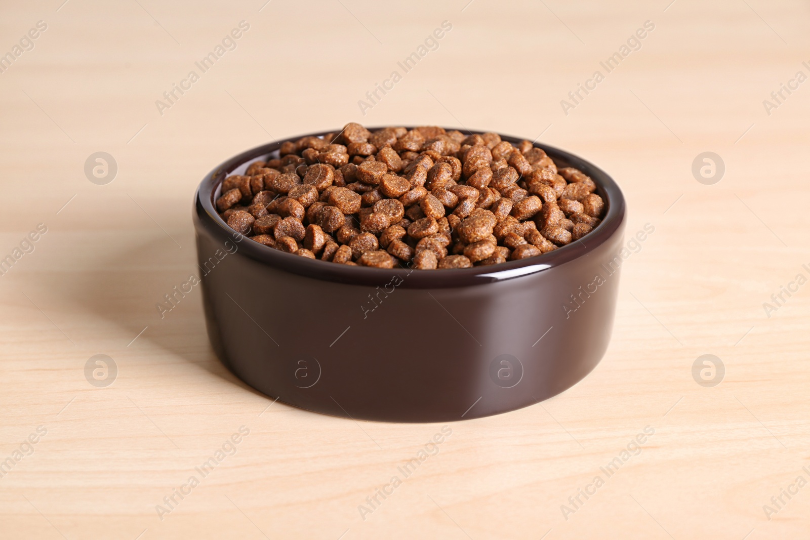 Photo of Dry dog food in pet bowl on wooden surface