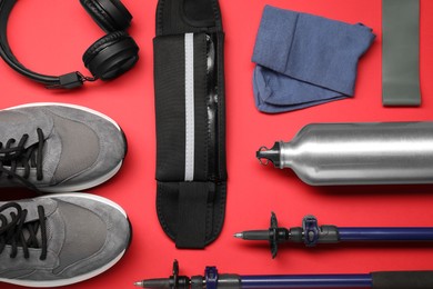 Photo of Sports equipment, sneakers, socks and headphones on red background, flat lay