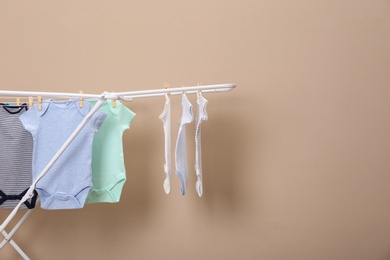 Photo of Different cute baby onesies hanging on clothes line against beige background, space for text. Laundry day