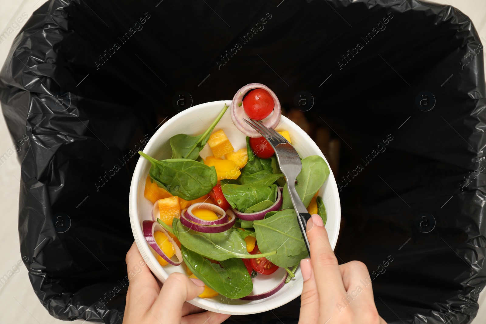 Photo of Woman throwing vegetable salad into bin indoors, top view