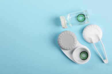 Photo of Bottle of solution, case with green contact lenses and tweezers on light blue background, flat lay. Space for text
