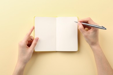 Photo of Woman writing in notebook on beige background, top view