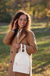 Beautiful African-American woman with stylish white backpack in autumn park