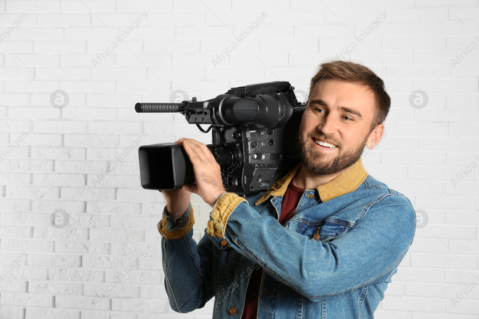 Photo of Operator with professional video camera near white brick wall