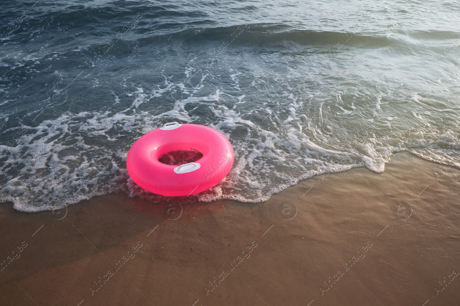 Photo of Bright pink inflatable ring on sandy beach near sea, space for text