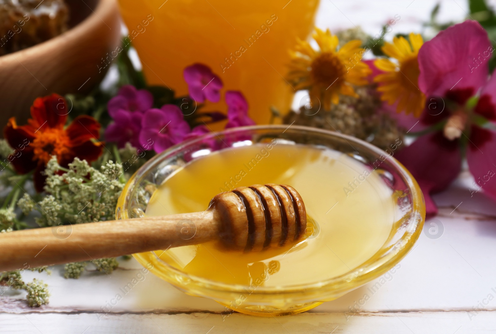 Photo of Honey with dipper in bowl and different flowers on white wooden table