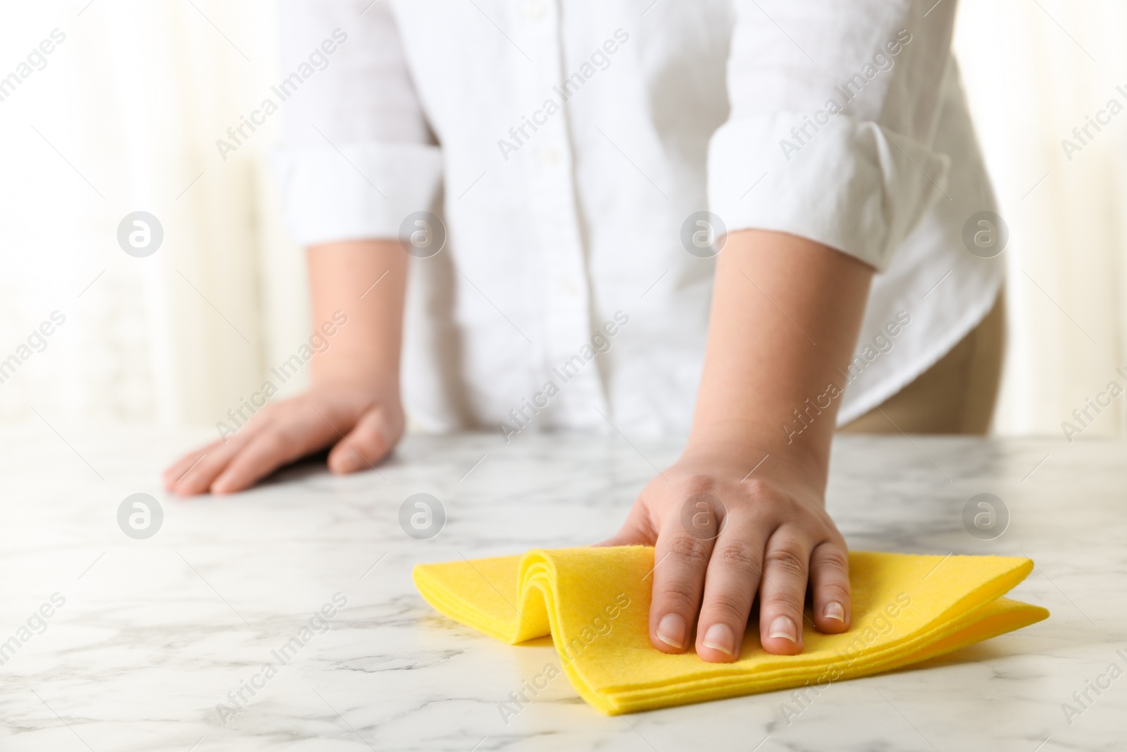 Photo of Woman wiping white marble table with rag indoors, closeup