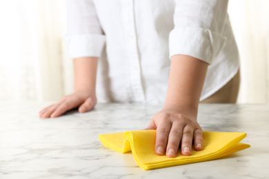 Photo of Woman wiping white marble table with rag indoors, closeup