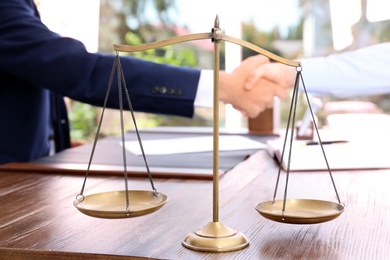 Photo of Scales of justice and blurred lawyer handshaking with client on background