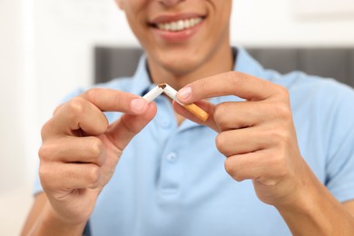 Stop smoking concept. Young man breaking cigarette on blurred background, closeup