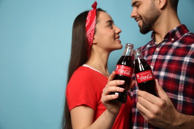 Photo of MYKOLAIV, UKRAINE - JANUARY 27, 2021: Young couple holding bottles of Coca-Cola against light blue background, closeup. Space for text