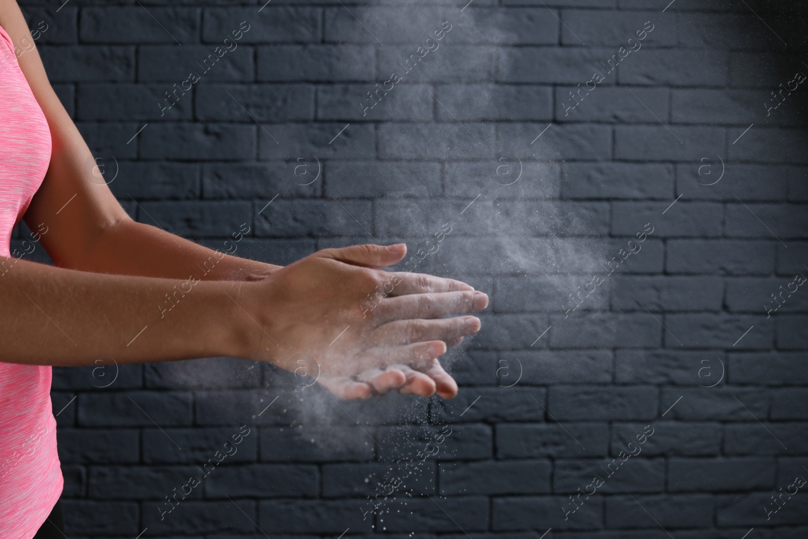 Photo of Young woman applying chalk powder on hands against brick wall