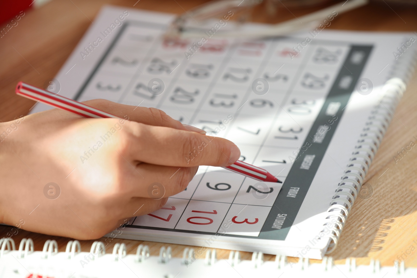 Photo of Woman marking date in calendar at wooden table, closeup