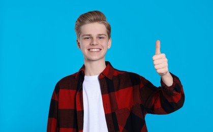 Teenage boy showing thumb up on light blue background