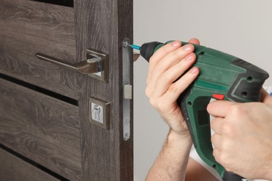 Photo of Worker with screw gun repairing door lock indoors, closeup