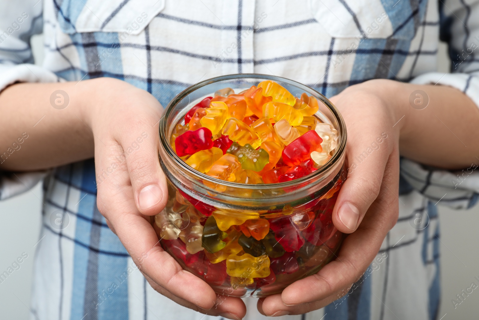 Photo of Woman holding jar of colorful jelly bears on light background, closeup