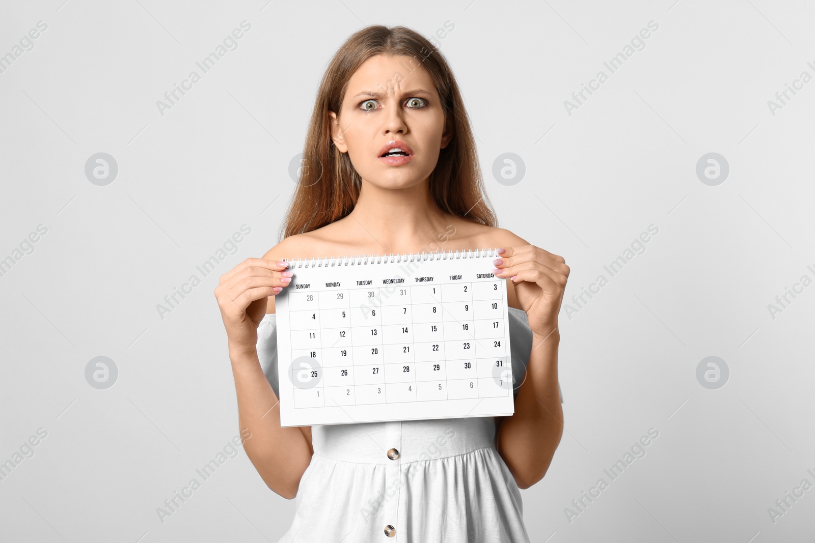 Photo of Emotional young woman holding calendar with marked menstrual cycle days on light background