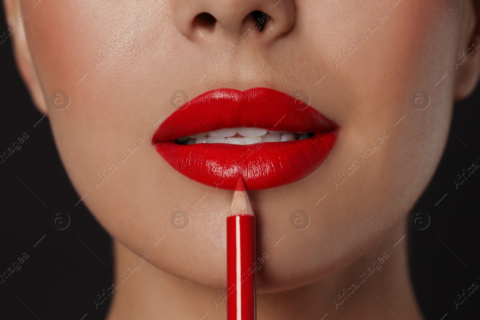 Photo of Young woman applying beautiful red lip pencil on black background, closeup