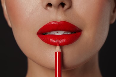 Young woman applying beautiful red lip pencil on black background, closeup